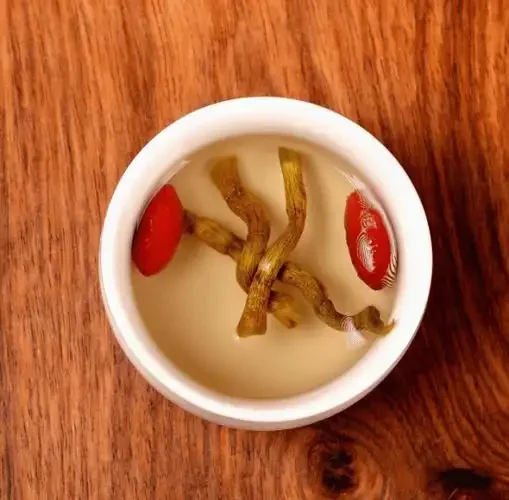 家庭自制铁皮石斛枸杞酒特写，玻璃罐中金黄酒液浸泡着红色枸杞和铁皮石斛，展示原料与成品状态。_1