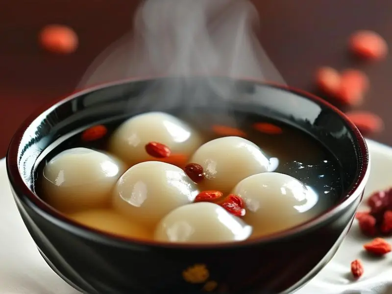 一碗美味的酒汤圆，汤圆饱满，酒汤清澈，点缀枸杞和桂花