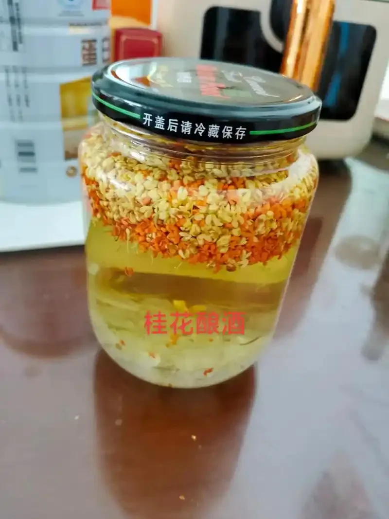 自制桂花酒成品展示：清澈的金黄色酒液与桂花在玻璃罐中分层，旁边摆放着新鲜的桂花、冰糖和基酒原料。_1