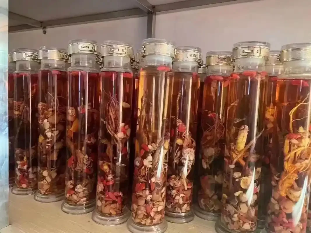 家庭自制补肾泡酒材料展示：透明玻璃瓶中浸泡着枸杞、桑葚等药材，旁边摆放着肉苁蓉、锁阳等原料。_1