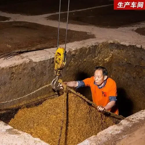 酿酒师傅正在翻动刚蒸好、冒着热气的高粱进行摊凉,背景是传统的酿酒工具,展现了粮食酒生产的关键环节。_1