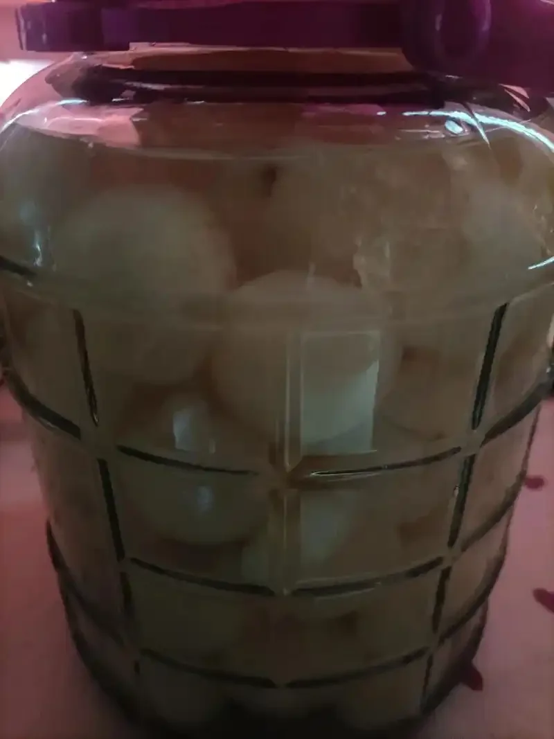 一瓶家庭自制的琥珀色水果泡酒,装在透明密封罐中,旁边散落着新鲜水果,展示果酒的自然色泽与状态。_1