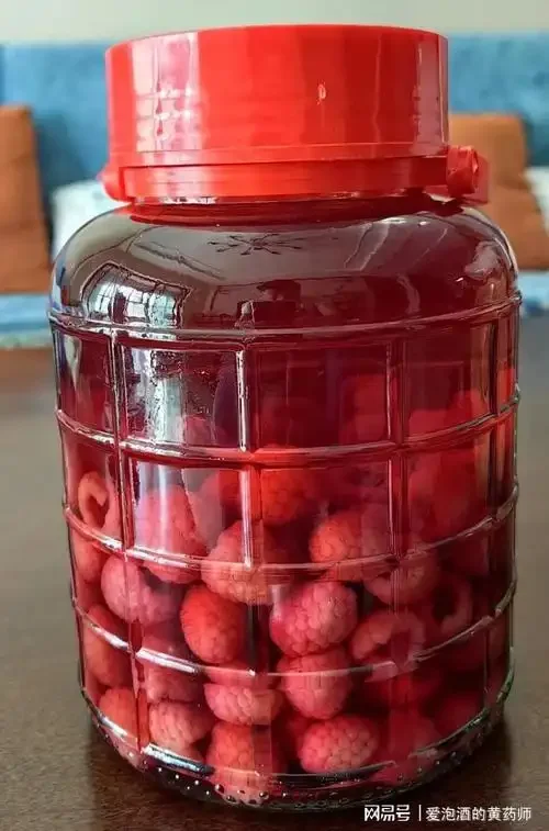 一个透明的玻璃泡酒罐特写，里面泡着红色的杨梅和枸杞，旁边放着一瓶清香型白酒和一些中药材，展示家庭泡酒的场景。_1