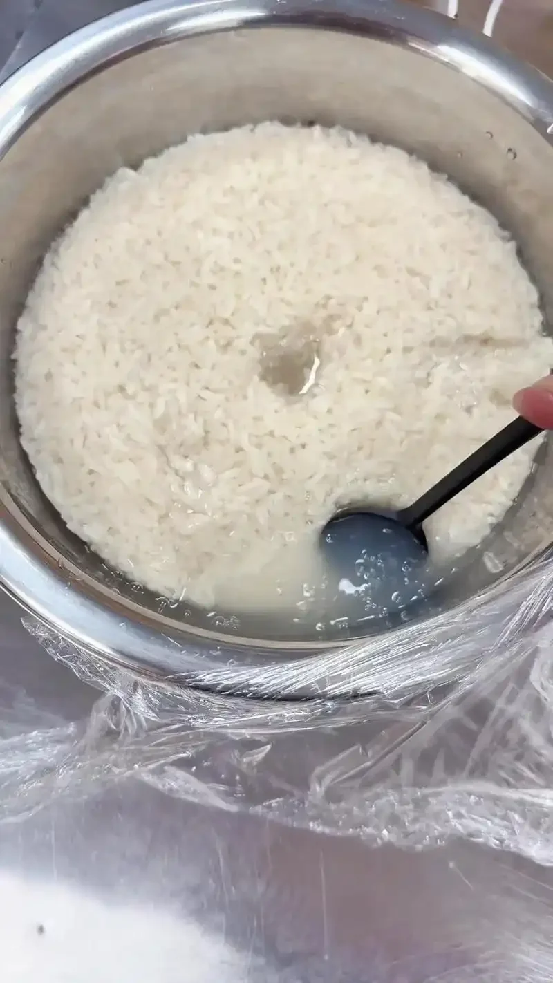 手工泡制酒米过程特写：手正在翻拌黄金小米与白酒，量杯显示约120ml酒液，体现传统制作工艺。_1