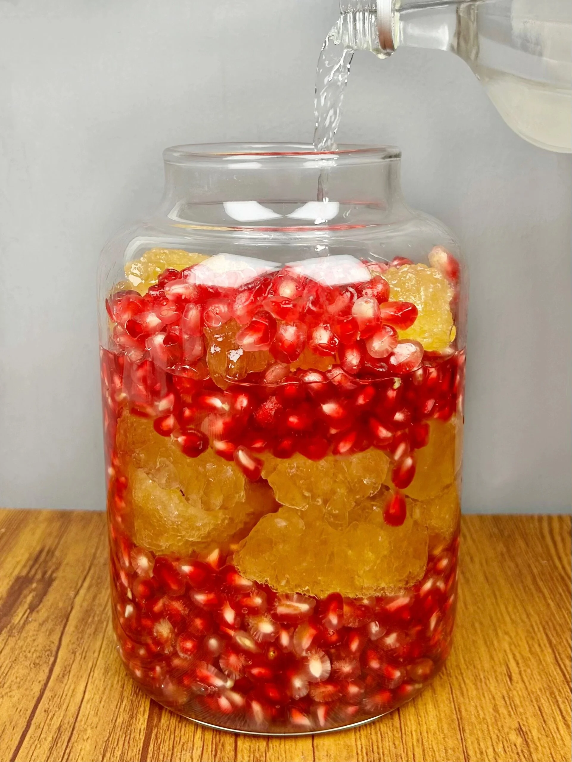 家庭自制酸石榴泡酒过程图，展示装有石榴籽和酒液的玻璃罐及所需材料_1