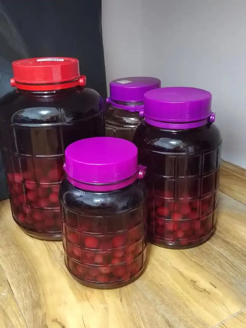 杨梅泡酒材料搭配展示：透明玻璃罐中的红色杨梅酒，旁边配有新鲜杨梅、冰糖、白酒瓶及柠檬片。_1