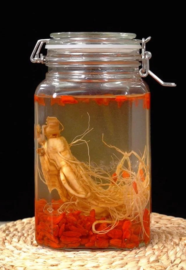 家庭自制人参泡酒成品展示：透明酒瓶中浸泡着完整人参、枸杞和红枣，酒液色泽金黄透亮。_1