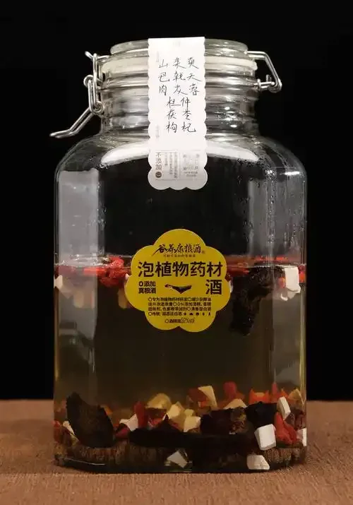 家庭自制山茱萸泡酒成品展示：玻璃瓶中琥珀色酒液与山茱萸果肉清晰可见，旁边散落着枸杞、黄芪等辅料。_1