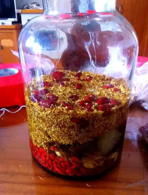 家庭自制桂花酒的材料准备与初步混合，玻璃罐中金黄色的酒液与桂花清晰可见。_1