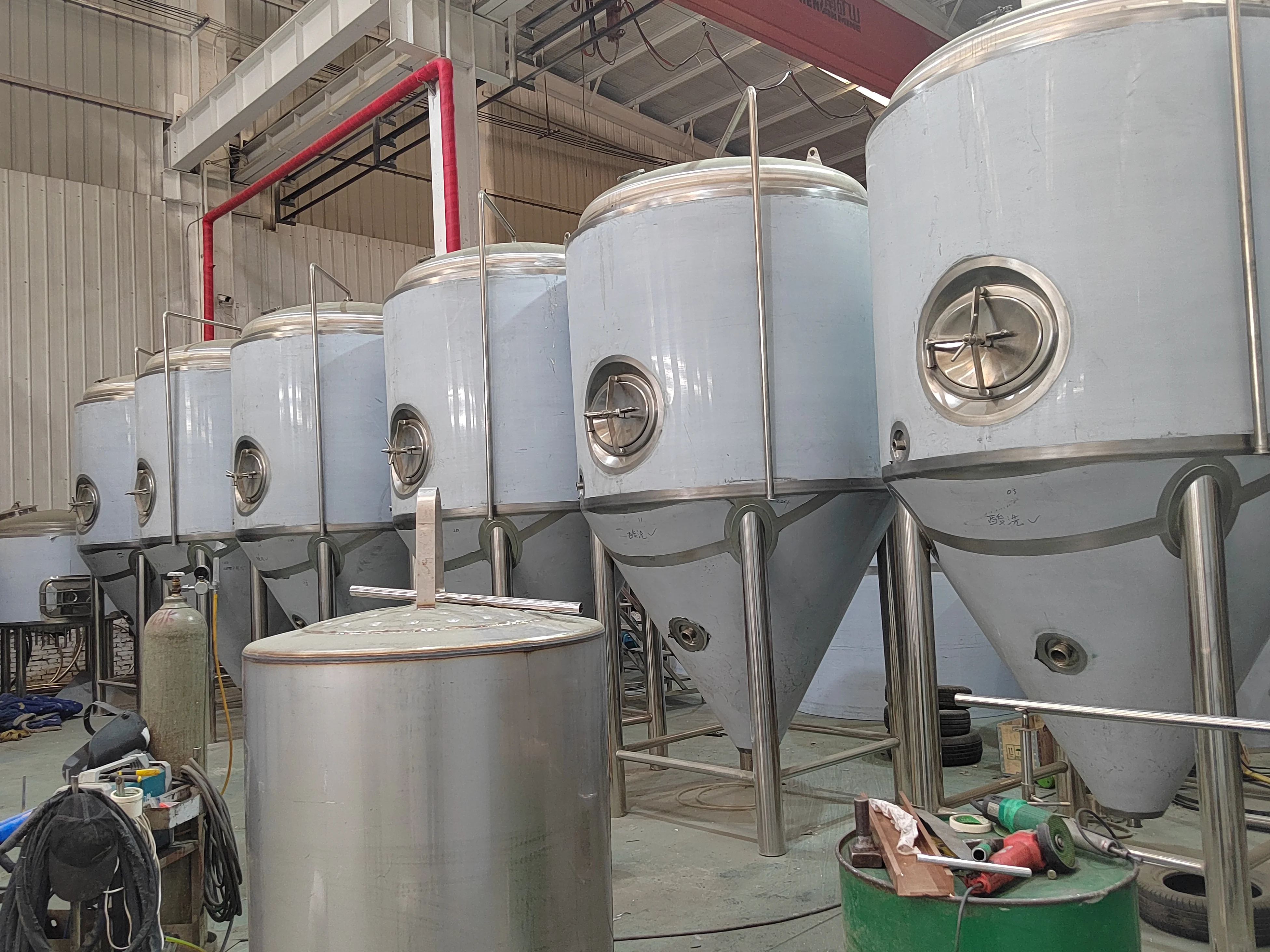 一套不锈钢精酿啤酒设备的糖化煮沸锅和发酵罐局部特写，背景是酿酒工作台。_1