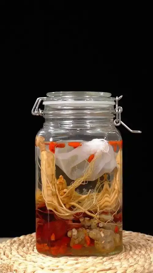鹿茸人参泡酒成品图：玻璃酒坛中金黄色的酒液，浸泡着人参和鹿茸切片，旁边搭配枸杞和红枣。_1
