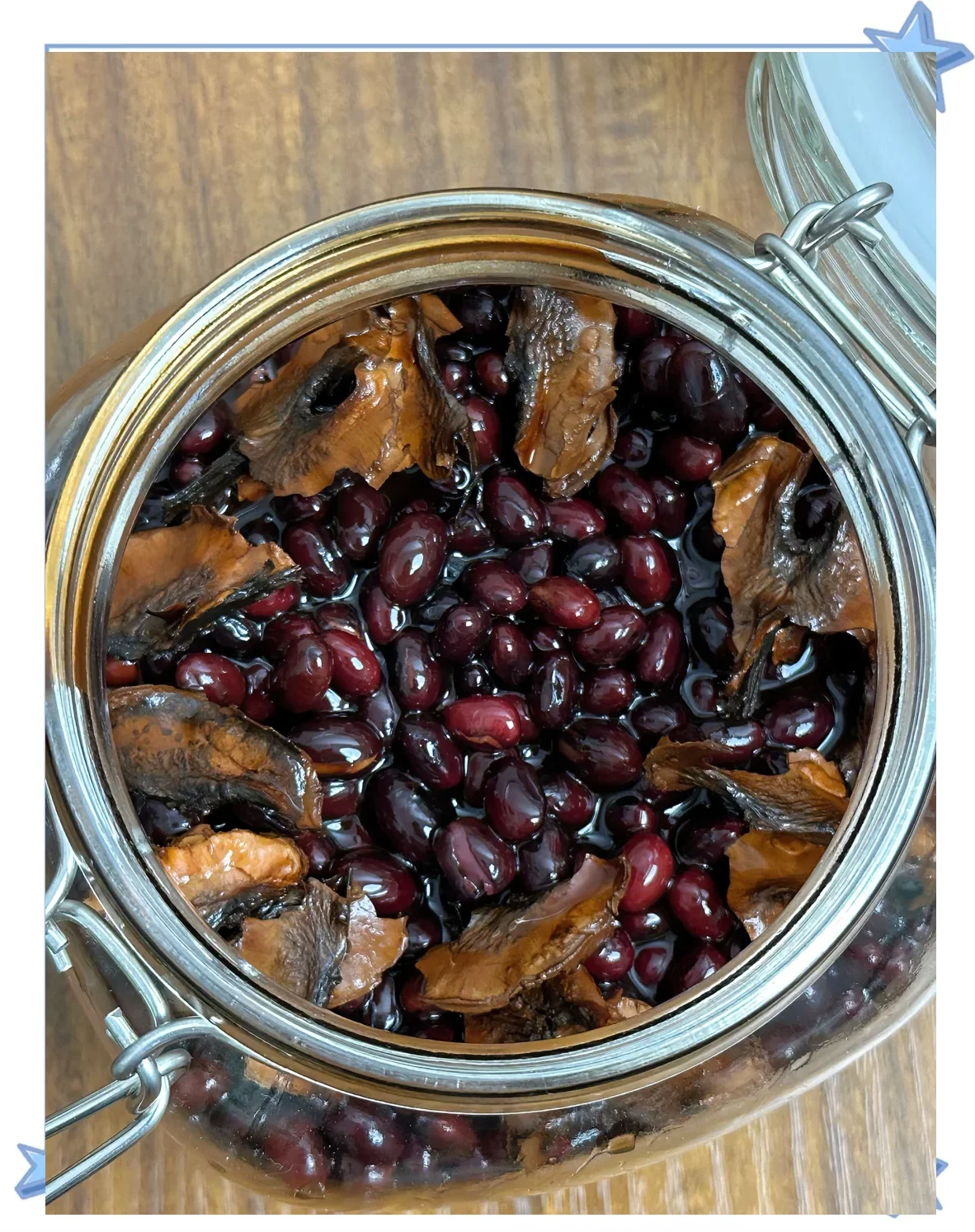 泡制完成的黑豆酒特写，酒体呈红褐色，黑豆沉底，旁边散落着原材料。_1