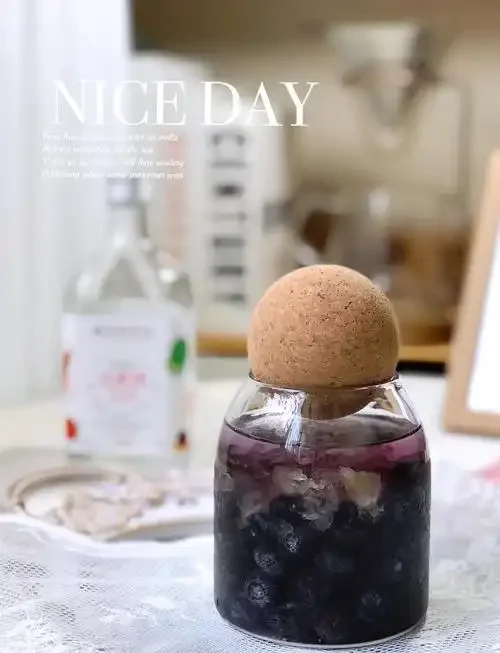 家庭自制蓝莓酒浸泡过程展示：玻璃罐中深紫色的蓝莓酒液与冰糖、果粒清晰分层，旁边摆放着新鲜蓝莓原料。_1