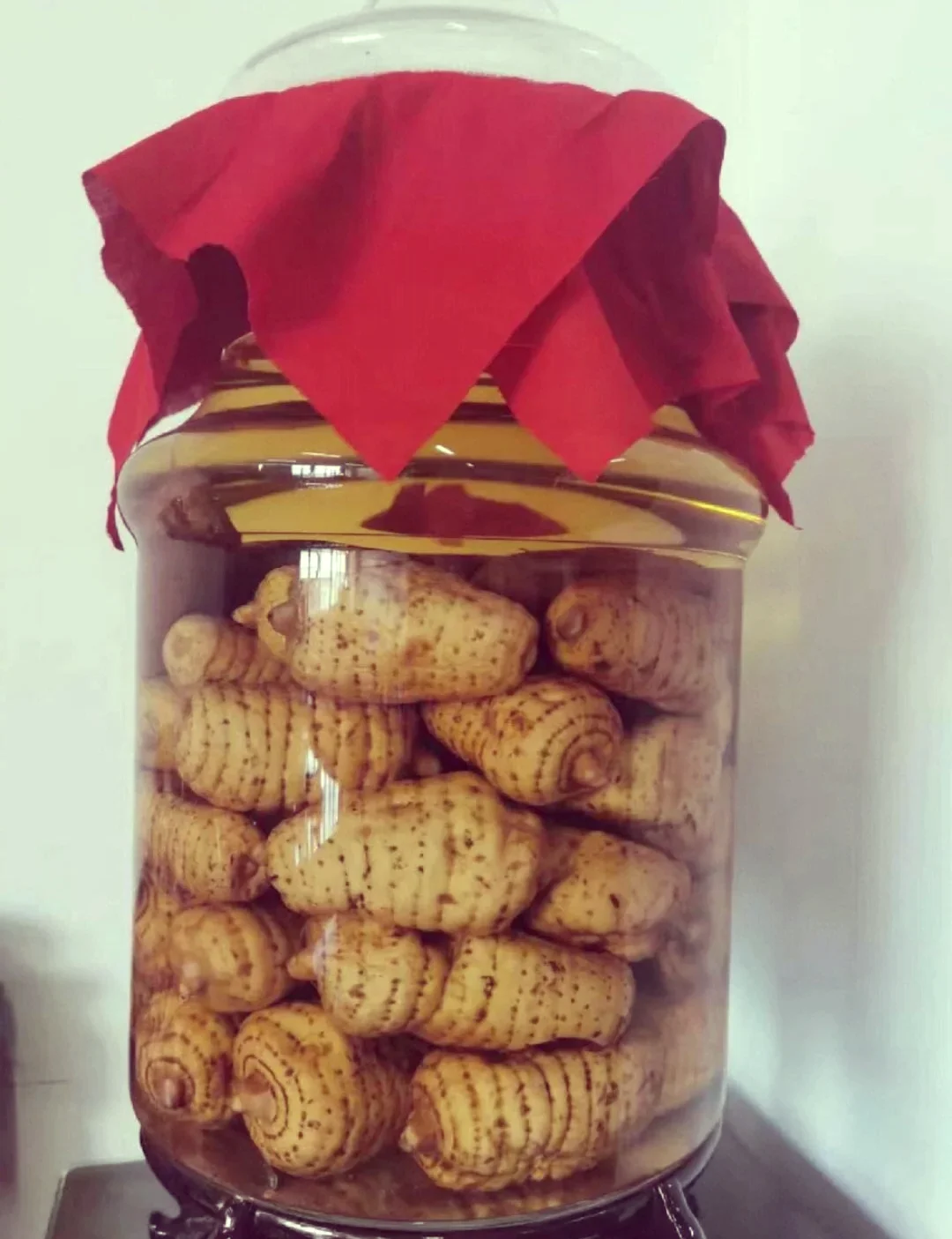 专业酿酒师展示天麻泡酒的成品与材料：一瓶清澈的琥珀色天麻酒、天麻切片和用于泡酒的纯粮白酒。_1