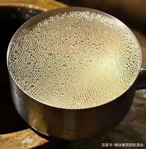 酿酒师的手将白酒倒入透明玻璃杯，杯中泛起密集细腻的酒花，用于展示如何观察酒花形态_1