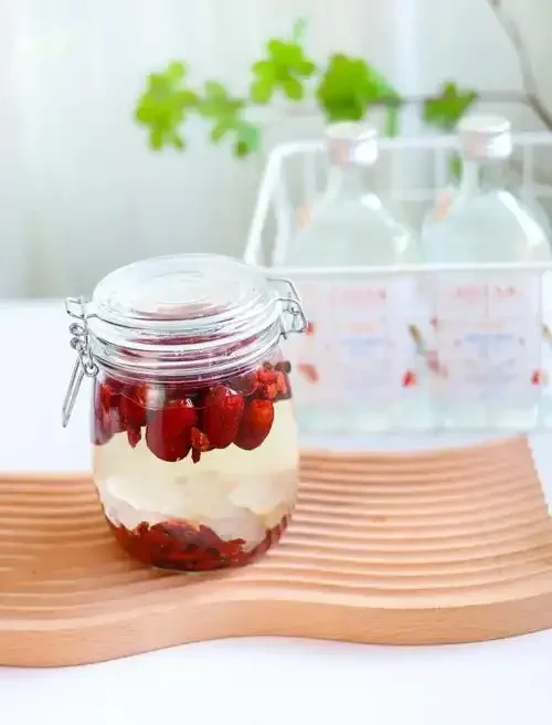 家庭自制的枸杞红枣泡酒，装在透明玻璃罐中，色泽红润透亮，配料清晰可见。_1