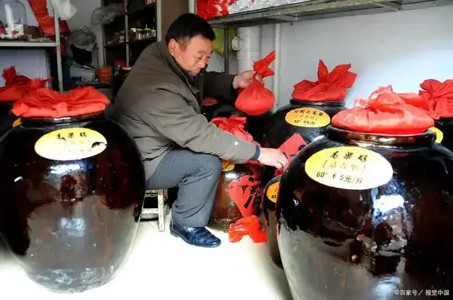 南楼山酿酒师在农村作坊向村民展示自酿的散装白酒，背景有发酵坛，场景温馨真实。_1