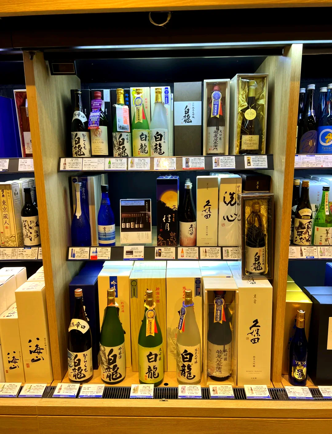 九种不同类型的日本清酒（日本酒）在木质桌面上的展示，包括纯米大吟酿、吟酿、本酿造等标签特写。_1