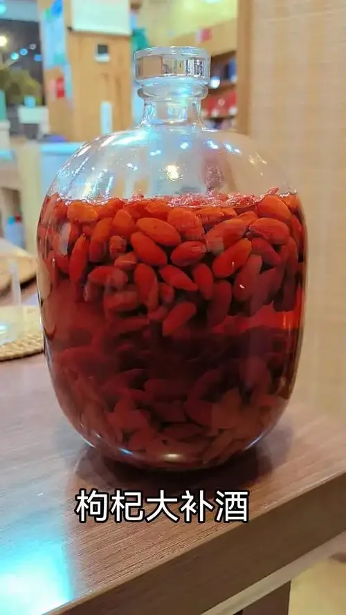 一罐清澈透亮的枸杞泡酒，里面泡着饱满的红色枸杞，旁边散落着干枸杞，光线温暖。_1