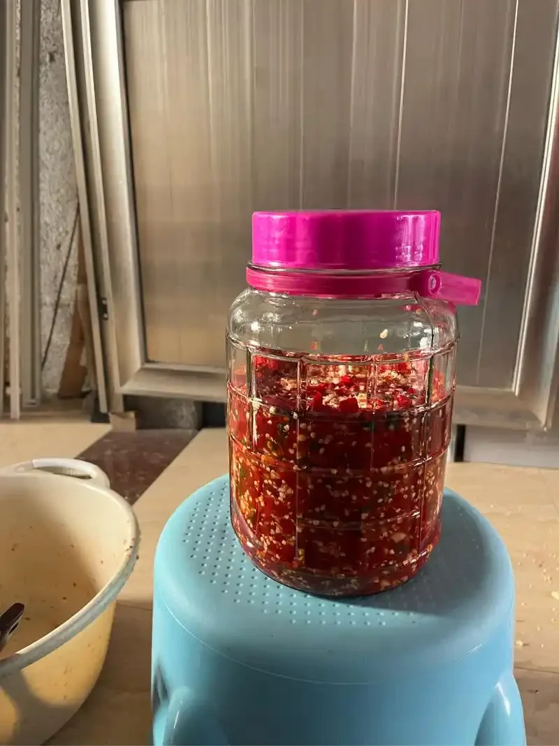 玻璃泡菜坛中腌制着鲜红的辣椒，旁边放着一小杯白酒和量杯，展示腌辣椒时添加白酒的正确场景_1