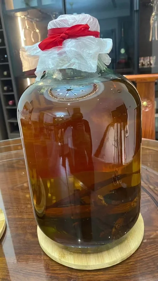 高丽参酒浸泡过程展示：透明酒坛，琥珀色酒液，高丽参，枸杞和冰糖等配料，旁边有小秤和手写笔记。_1