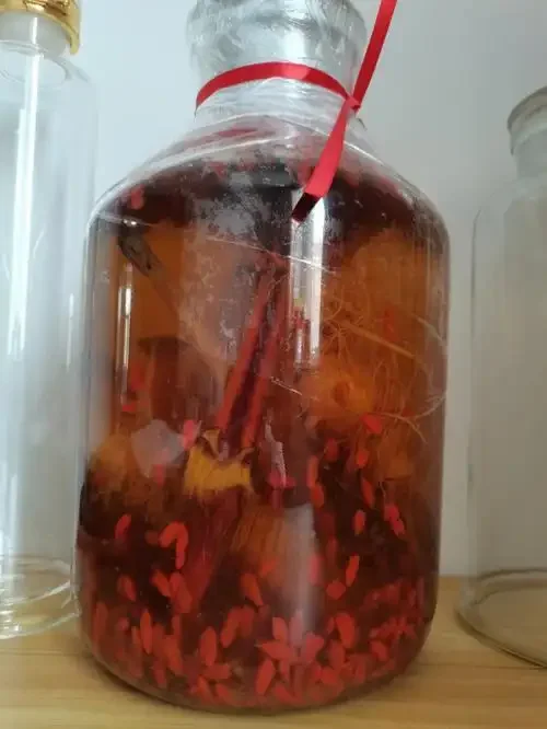 展示人参鹿茸泡酒成品静物图，透明玻璃罐中可见人参、鹿茸片和金黄色酒液。_1