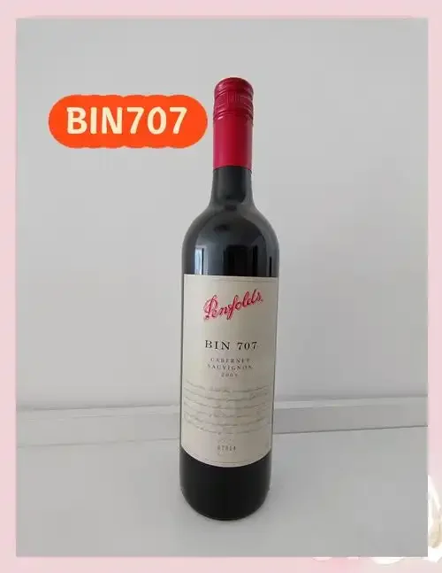 一瓶奔富Bin 707红酒与酒杯，背景为酒窖橡木桶，展示顶级澳洲赤霞珠的优雅形态。_1