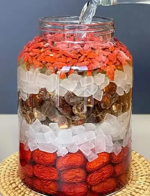 红枣、枸杞、桂圆在玻璃罐中泡酒的特写照片，展示家庭自制养生酒的过程。_1