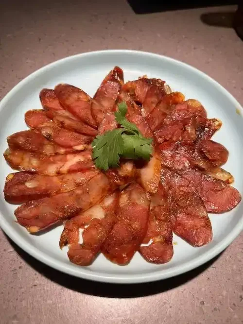腊肉腌制过程特写：五花肉块被抹上酱料，旁边有花椒、八角等香料和一瓶高度白酒。_1