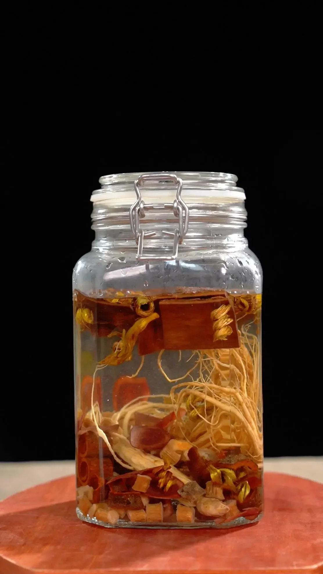 一个装有金黄色药酒的透明玻璃罐，罐内可见皂角刺等药材，旁边散落着干皂角刺和八角，置于木桌上，光线自然温暖。_1