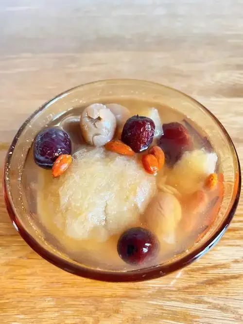 雪莲枸杞泡酒材料展示：玻璃罐中浸泡的雪莲花与枸杞特写，旁边摆放着待用的干燥雪莲、枸杞及一瓶纯粮食白酒。_1