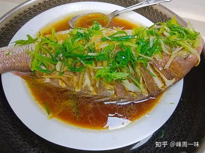 清蒸鲈鱼在蒸锅中，旁边放有姜葱和一瓶黄酒，展示蒸鱼放酒去腥增鲜的实际场景。_1