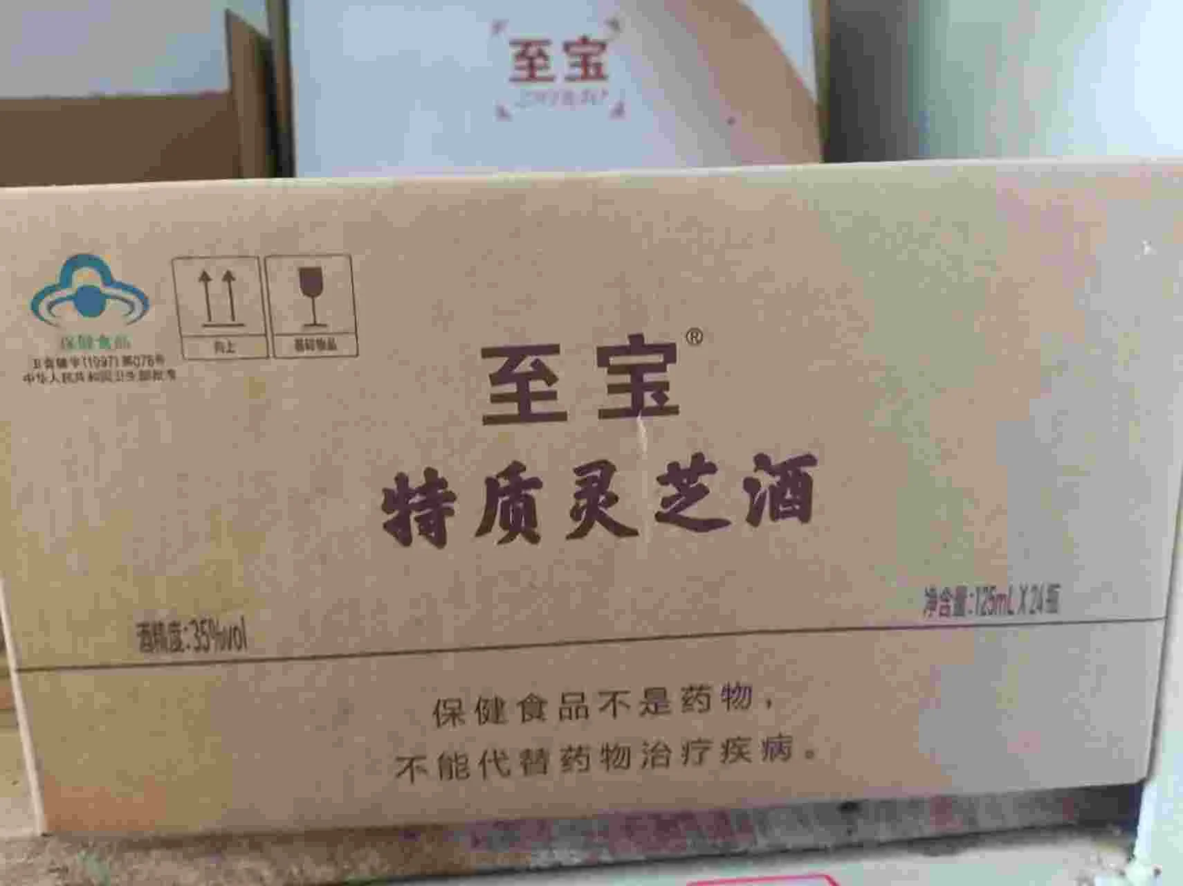 一瓶琥珀色的至宝灵芝酒特写，瓶中可见完整灵芝，旁边搭配枸杞和人参切片，背景为木质桌面。_1