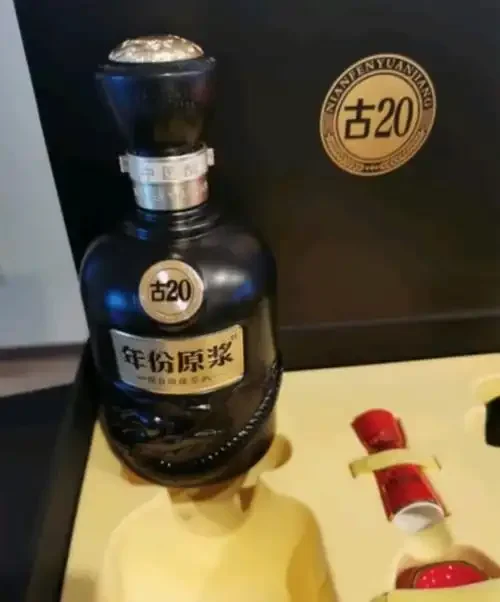 一瓶标签有岁月感的20年陈酿古酒静置于木桌上，旁有酿酒谷物与酒杯，光线柔和，氛围沉稳。_1