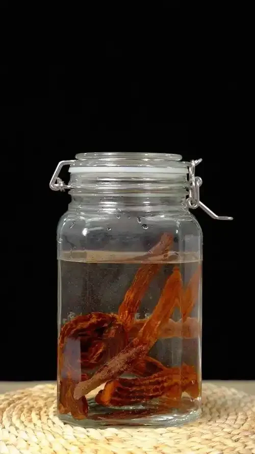 百部泡酒制作过程展示：玻璃瓶中琥珀色药酒与百部切片，旁边的中药秤和陶瓷酒壶_1