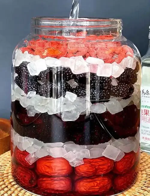 泡在透明玻璃罐中的深紫红色桑葚干酒，旁边有桑葚干、冰糖和白酒瓶，展示家庭酿酒过程_1
