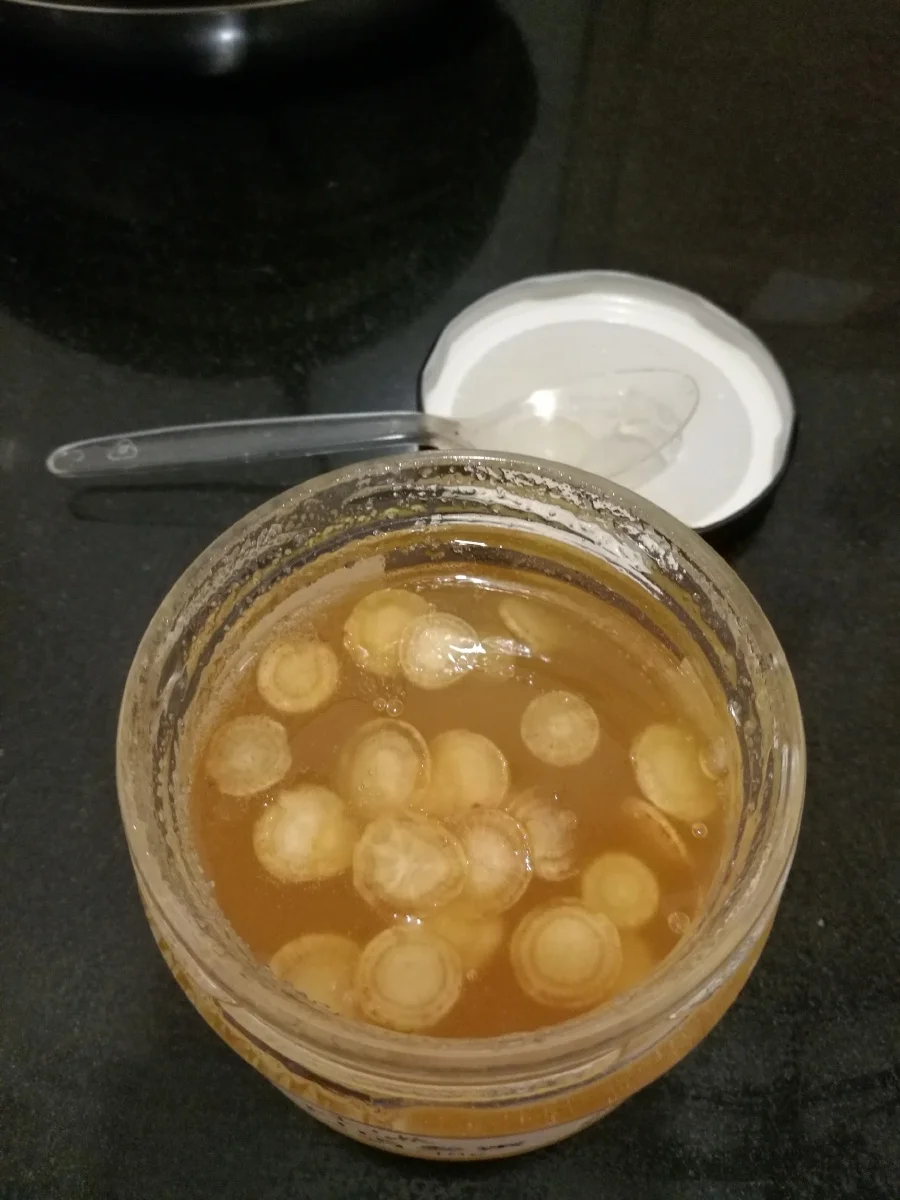人参蜂蜜泡酒制作过程特写：玻璃罐中的人参与琥珀色酒液，蜂蜜正被加入。_1