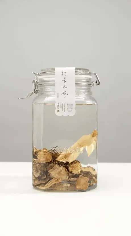 透明玻璃罐中浸泡的玛卡酒,酒液呈深琥珀色,可见玛卡切片和枸杞,旁边放有干玛卡原材料。_1