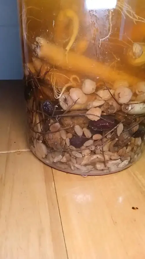 鹿茸和韭菜子泡酒的家庭泡制场景特写：透明酒坛中金黄色的酒液浸泡着鹿茸片与韭菜子，旁边散落着原材料和配方纸，背景为木质酒架。_1