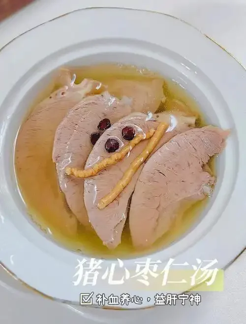 一碗炖好的酒炖猪心特写，汤汁浓郁，配料清晰可见，旁边伴有酒壶和药材，展现传统食补的温馨场景。_1
