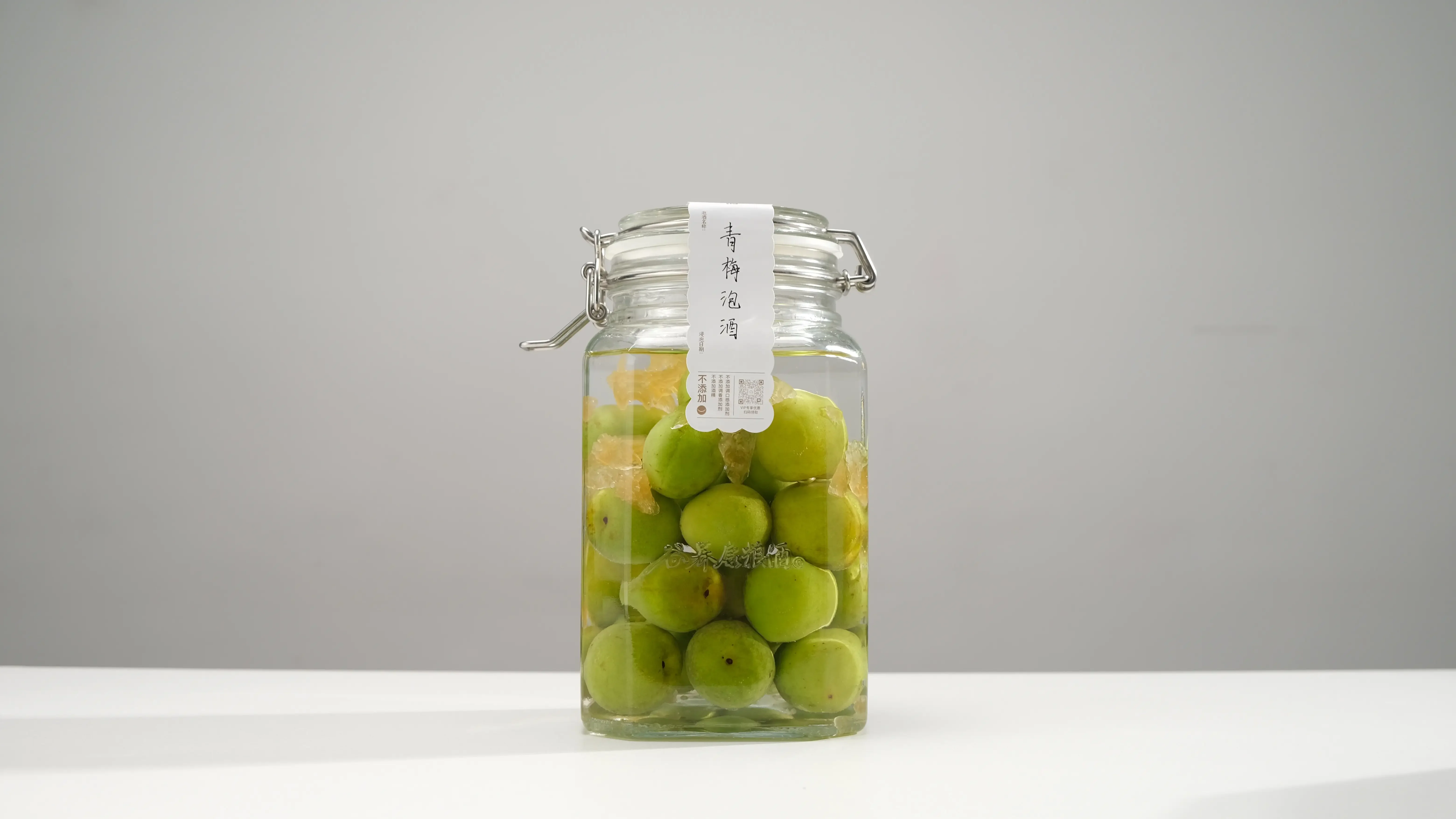 家庭自制青梅酒所需材料展示：透明玻璃罐中琥珀色的青梅酒、新鲜青梅、冰糖和一瓶纯粮白酒_1