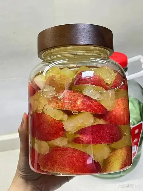 水蜜桃泡酒制作过程：透明玻璃罐中正在浸泡的水蜜桃块与冰糖_1