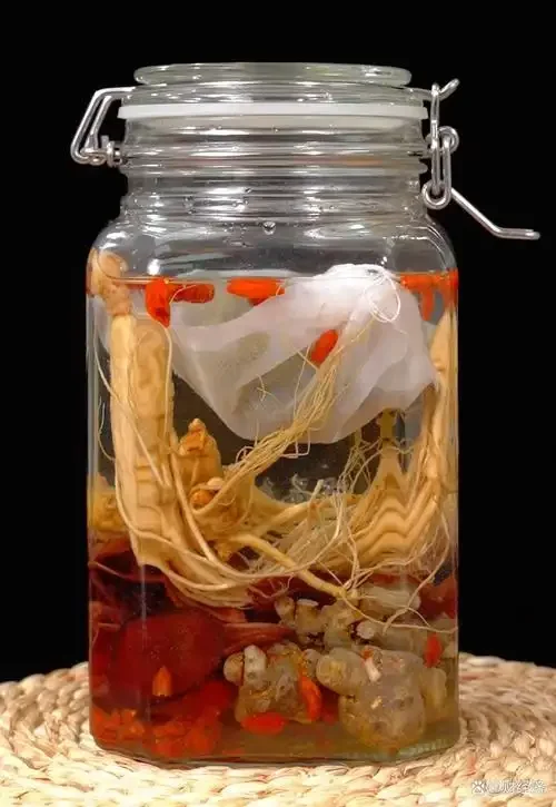 浸泡中的人参鹿鞭酒特写，玻璃酒坛内可见整支人参和鹿鞭切片，酒色琥珀通透，旁边摆放着未浸泡的原料。_1