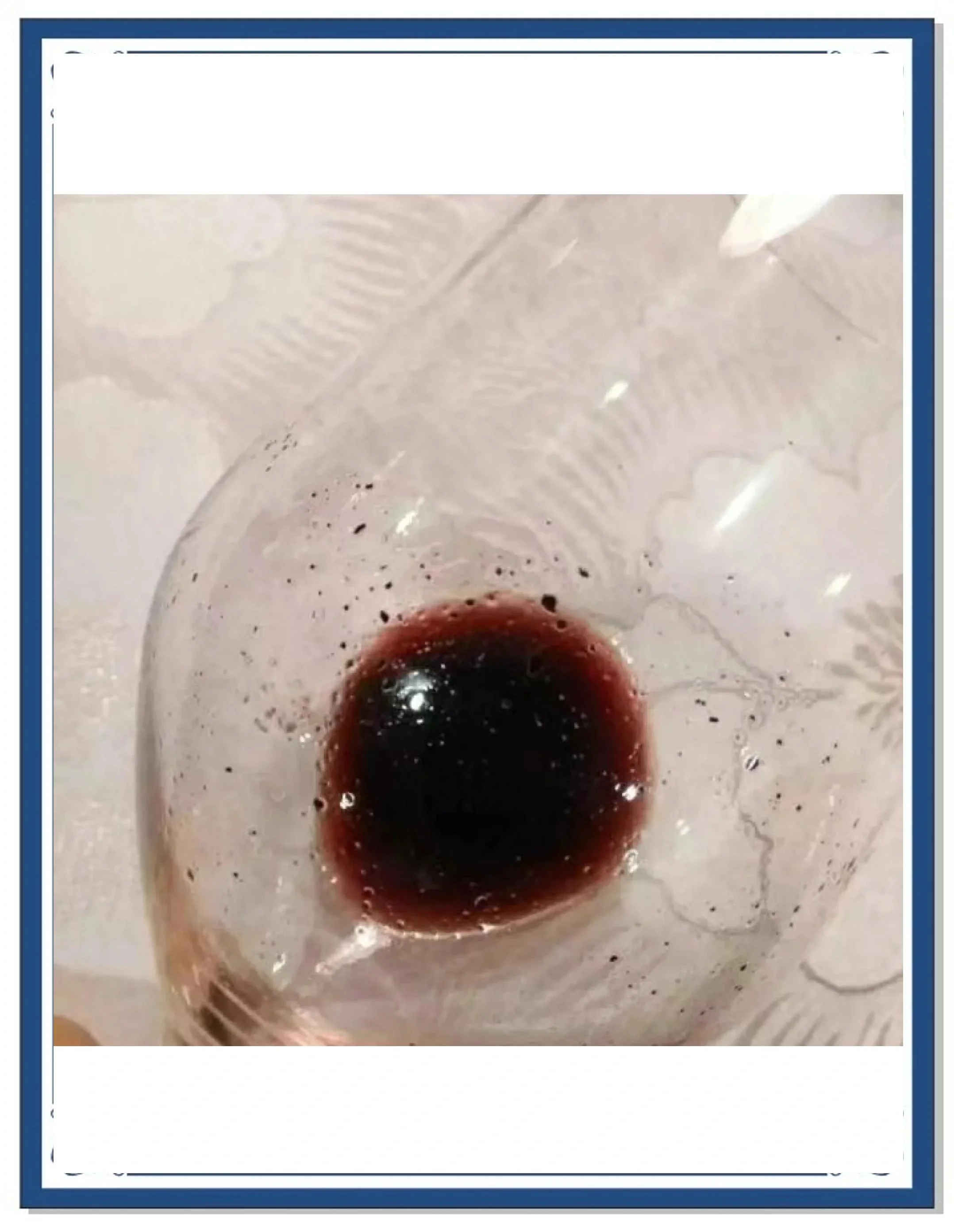 一瓶红葡萄酒瓶底可见深红色沉淀物的特写照片，旁边放着一个空酒杯，背景为酿酒环境。_1