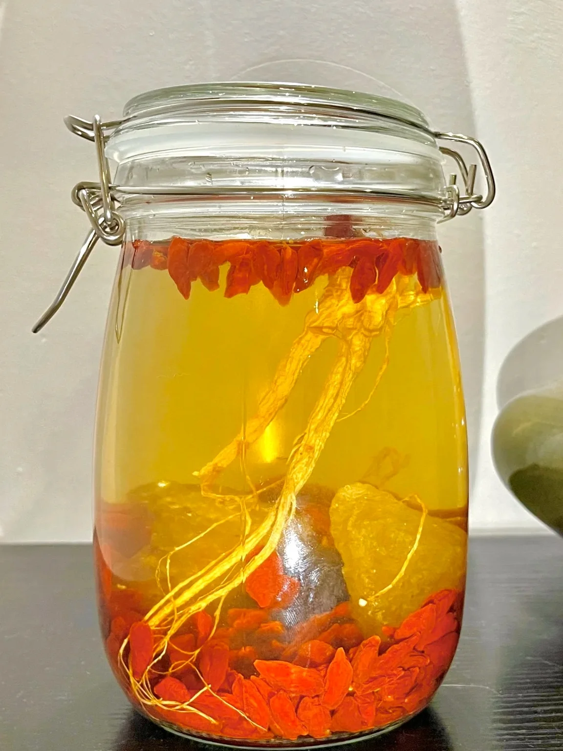 人参、枸杞、黄芪在透明玻璃罐中浸泡于白酒中的特写照片，展示自制养生药酒的过程。_1