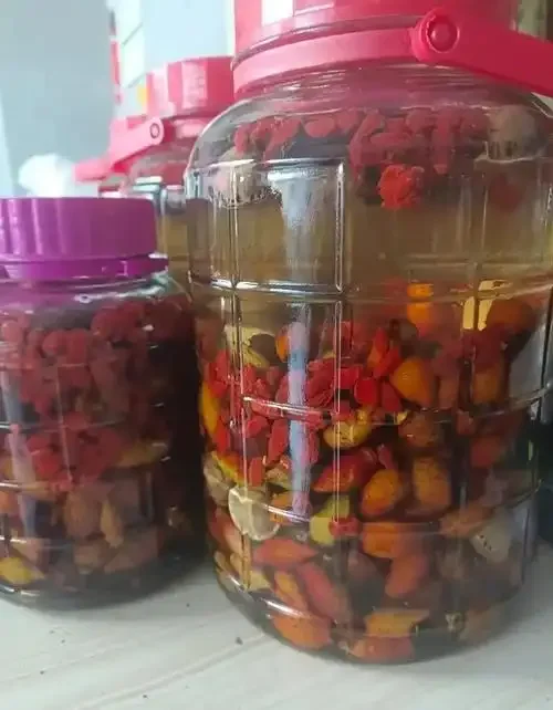 枸杞子和金樱子共同浸泡在透明玻璃罐的白酒中，展示家庭自制养生酒的和谐搭配_1