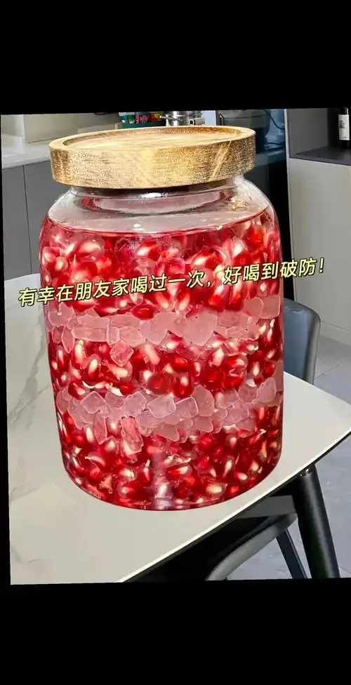 家庭自酿石榴酒特写：玻璃罐中宝石红色的酒液正在发酵，旁边是新鲜切开的红石榴籽_1