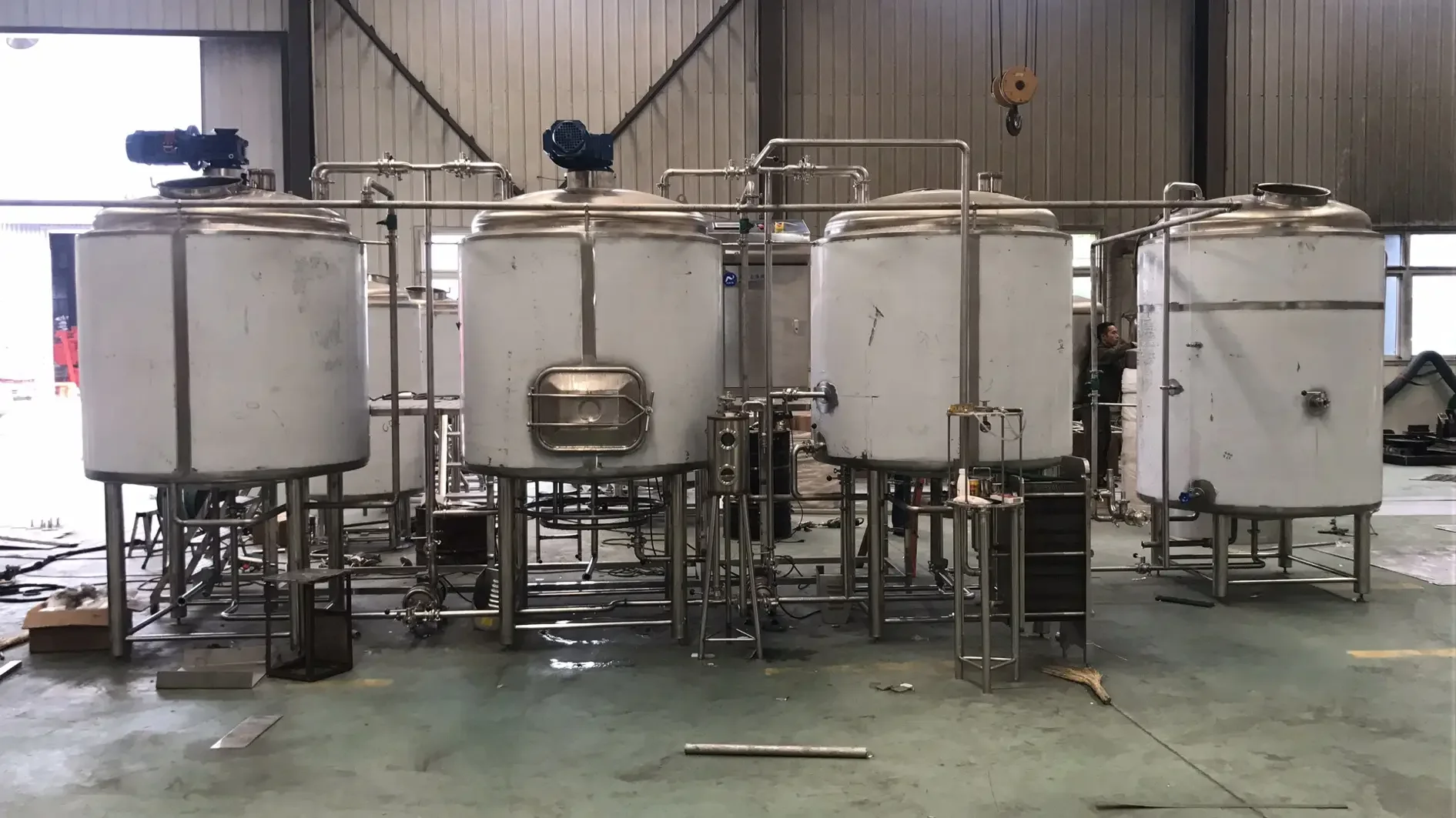 家庭工作坊中的不锈钢微型啤酒酿造设备,旁边摆放着麦芽、啤酒花和成品啤酒,适合家庭自酿使用。_1