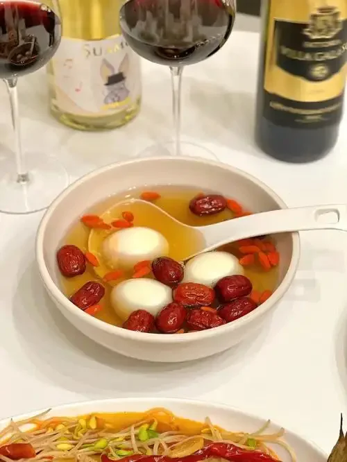 一碗热腾腾的米酒煮蛋，蛋花柔软，汤汁清澈，点缀着红色枸杞和黄色桂花，看起来温暖诱人。_1